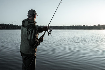 Male fisherman at dawn on the lake catches a fishing rod. Fishing hobby vacation concept. Copy space.