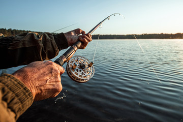 Hands of a man in a Urp plan hold a fishing rod, a fisherman catches fish at dawn. Fishing hobby...