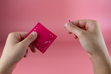 Young girls hands poking a hole in a condom with a needle, infidelity concept, getting pregnant