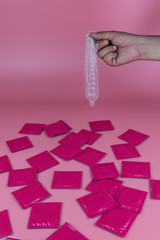 Young  man holding a condom on a pink background with pink condoms on the table, concept, fertility, sexual health