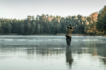 A male fisherman on the lake is standing in the water and fishing for a fishing rod. Fishing hobby vacation concept. Copy space.