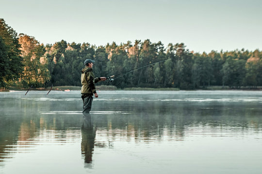 A male fisherman on the lake is standing in the water and fishing for a fishing rod. Fishing hobby vacation concept. Copy space.