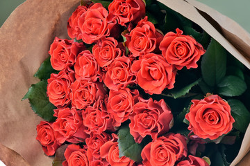 Bouquet beautiful red roses with selective focus in craft paper. Luxury bouquet made of amazing red roses. Valentines Bouquet of red roses. Present for Mother’s Day.  Close-up of red roses bouquet. 