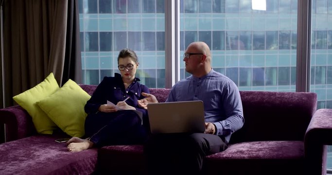 bald man is speaking with his young wife sitting in apartment in daytime, woman is writing