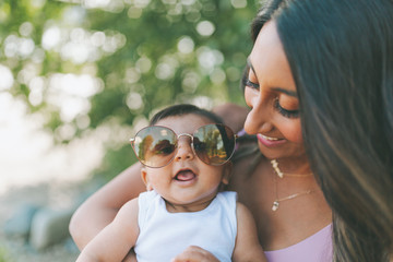 A mother and baby wearing sunglasses at the beach