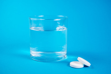 Clear glass of water and soluble effervescent tablets isolated on blue background. The concept of treatment and prevention of viral diseases. Help with depression and insomnia.To drink liquid medicine