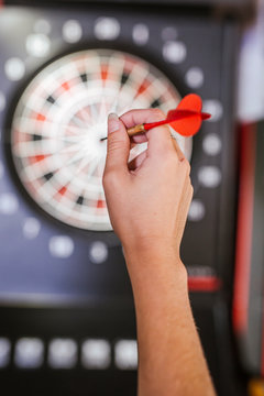 Close-up of woman's hand holding dart in front of dartboard