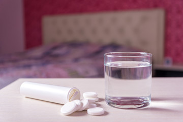 A glass of water and a tube of soluble effervescent tablets on the blurred background of the bed in the bedroom.Treatment and prevention of viral diseases. Help with depression and insomnia.copy space