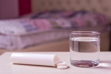 A glass of water and a tube of soluble effervescent tablets on the blurred background of the bed in the bedroom.Treatment and prevention of viral diseases. Help with depression and insomnia.copy space