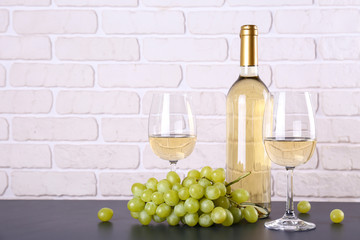 Vintage bottle of white wine without label, two glasses and bunch of grapes on wooden table, lofty...
