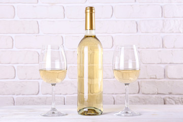 Vintage bottle of white wine without label, two glasses and bunch of grapes on wooden table, lofty white brick wall background. Expensive bottle of chardonnay concept. concept. Copy space.
