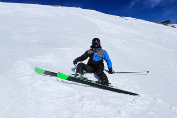 Pro skier in winter outfing lying or sitting in white snow with his black and green skis. Male...