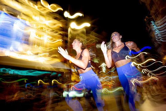 Long exposure photo of two women running in the city at night