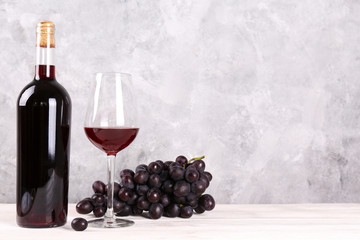 Vintage bottle of red wine without label, a glass and bunch of grapes on wooden table, grunged...