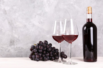 Vintage bottle of red wine without label, two glasses and bunch of grapes on wooden table, grunged...