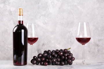 Obraz premium Vintage bottle of red wine without label, two glasses and bunch of grapes on wooden table, grunged concrete wall background. Expensive bottle of cabernet sauvignon concept. Copy space,