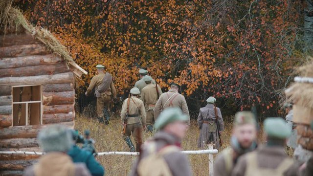 Men soldiers in warm coats walking in autumn nature - field and forest - Reconstruction of a hostilities