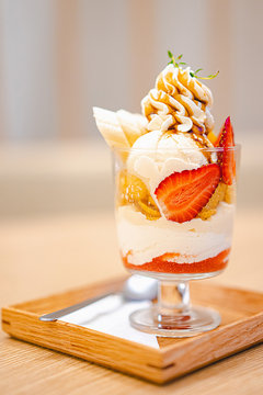 Vanilla parfait with strawberries and banana served in a glass on top of a wood plate.