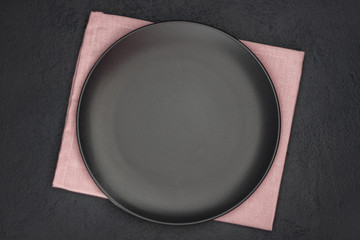 Black plate, cutlery and napkin on stone table top view. Table setting.