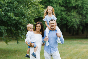 Fototapeta premium Portrait of a beautiful family: mom, dad, two-year-old son and five-year-old daughter. Parents hold children in their arms. The family is dressed in blue and white clothes