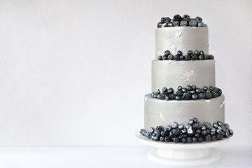 Wedding cake with silver cream, decorated with blueberries and blackberries on a white wooden...