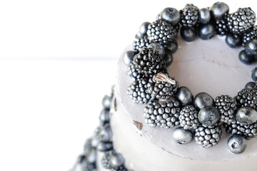 Wedding cake with silver cream, decorated with blueberries and blackberries on a white wooden background. Three-tiered, beautiful decor. Top view.