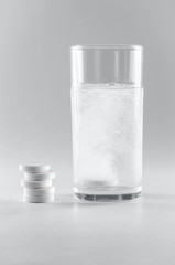 The effervescent tablet dissolves in a glass of water. A stack of drugs isolated on a white background. Treatment of viral diseases. Help with depression and insomnia. Liquid multivitamins