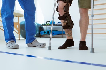 Man after car accident in an orthosis and on crutches learning to walk in the clinic, helpful...