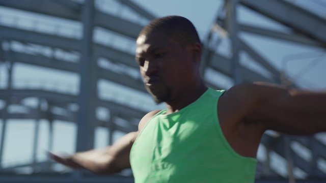 Zoom in closeup shot of well-muscled African athlete doing warm up arm exercise standing on urban bridge