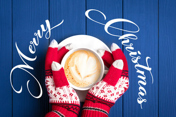 female hands with knitted gloves with New Year's pattern hold white cup with hot coffee cappuccino...