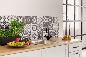 Herbs and fruits on kitchen counter in bright kitchen interior with trendy tiles on the wall - obrazy, fototapety, plakaty