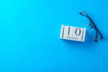Glasses and wooden calendar, world view day, concept, on blue background, top view