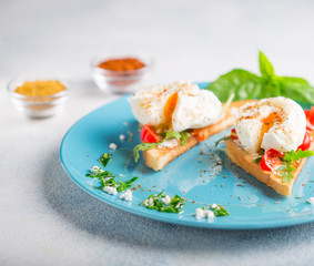 Triangular toast with poached egg on a large blue plate with green sauce and spices copy space