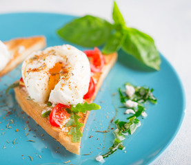 Triangular toast with poached egg on a large blue plate with green sauce and spices copy space