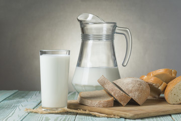 Glass of milk, jug and slices of fresh bread on a wooden board