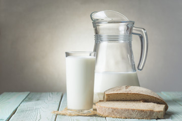 Glass of milk, jug and slices of fresh bread on a wooden board, on bright background