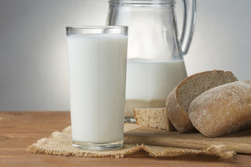 Glass of milk, jug and slices of fresh bread on a wooden board, closeup
