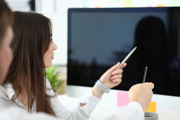 Portrait of smart businessman and businesswoman sitting in modern workplace and pointing at...