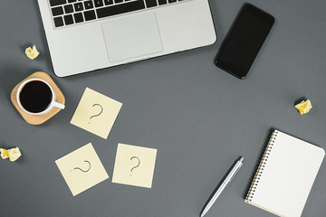 Question mark on sticky notes, notebook, cup coffee, phone, pen on gray background. FAQ concept....