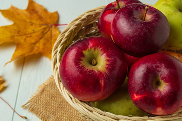 Still life with a view of autumn apples in a basket and maple leaves, closeup