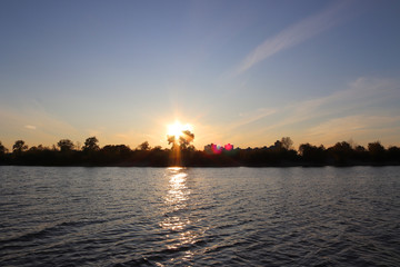 Wonderful sunset on the river or lake. On the horizon are silhouettes of trees and city buildings. Calming atmosphere