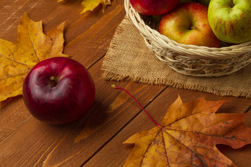 Red apple and maple leaves on a wooden background