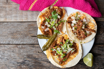 Mexican birria tacos with onion and cilantro on wooden background