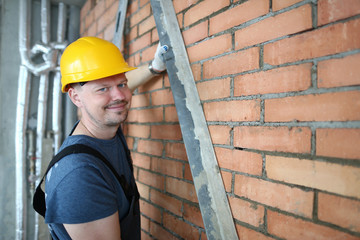Portrait of constructor making brick wall smooth in order to plastering brick wall. Smiling...