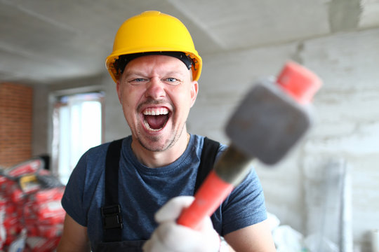 Portrait of screaming male holding big sturdy construction tool. Scary builder laughing at camera with joy and madness. Strange guy wearing yellow hardhat and bricklayer outfit. Building concept