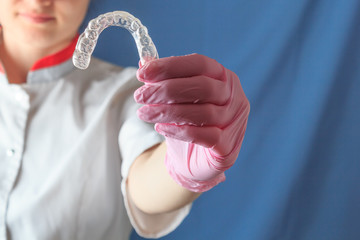 Female dentist holding mouth guard for teeth whitening, on blue background