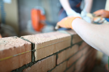 Close-up of skilled builder wearing special gloves to protect arms. Experienced constructor with hammer to lay red bricks and make big masonry perfect. Building concept