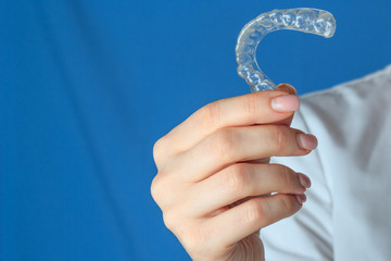 Female dentist holding mouth guard for teeth whitening, on blue background, close-up