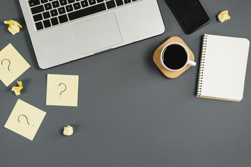 Question mark on sticky notes, notebook, cup coffee, phone, pen on gray background. FAQ concept....