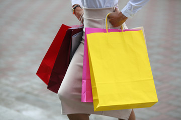 Close-up of female hands with colorful packages walking down street. Beautiful woman wearing business style clothes. Fashion and shopping concept. Blurred background